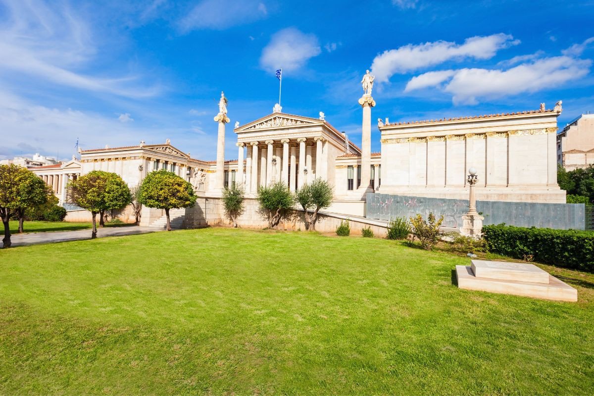 The Academy of Athens with statues and greenery under a clear sky.